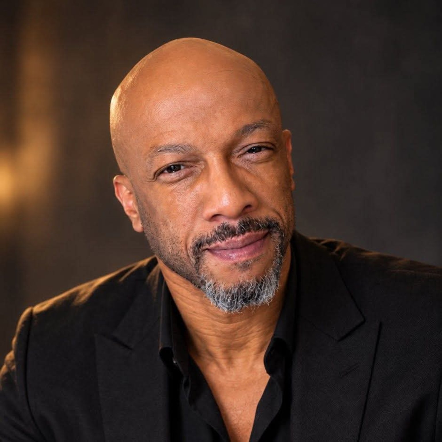 Professional portrait of Rev. Dr. Christian Frazier wearing a black blazer against a warm dark background
